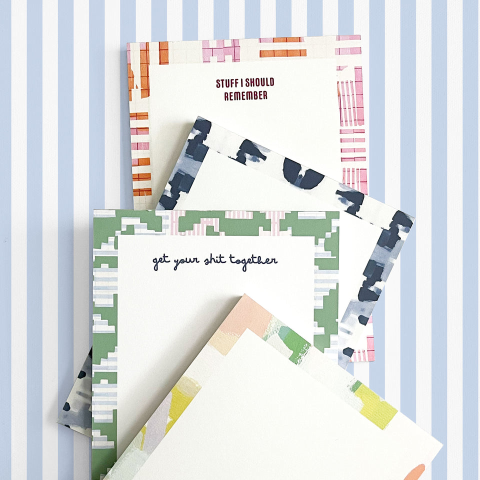 Stack of colorful 5x7 custom notepads with patterned borders, shown on a light purple and white striped background. Visible headers read ‘STUFF I SHOULD REMEMBER’ in red text and ‘get your shit together’ in navy script.